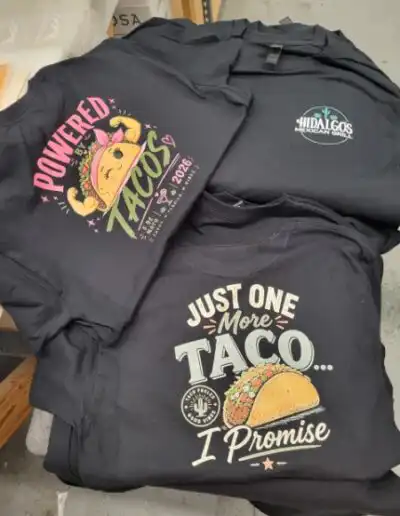 Dark grey T-Shirts for Hildalgo's Mexican Grill celebrating Cinco De Mayo with the name on the front pocket and a taco and slogan on the back