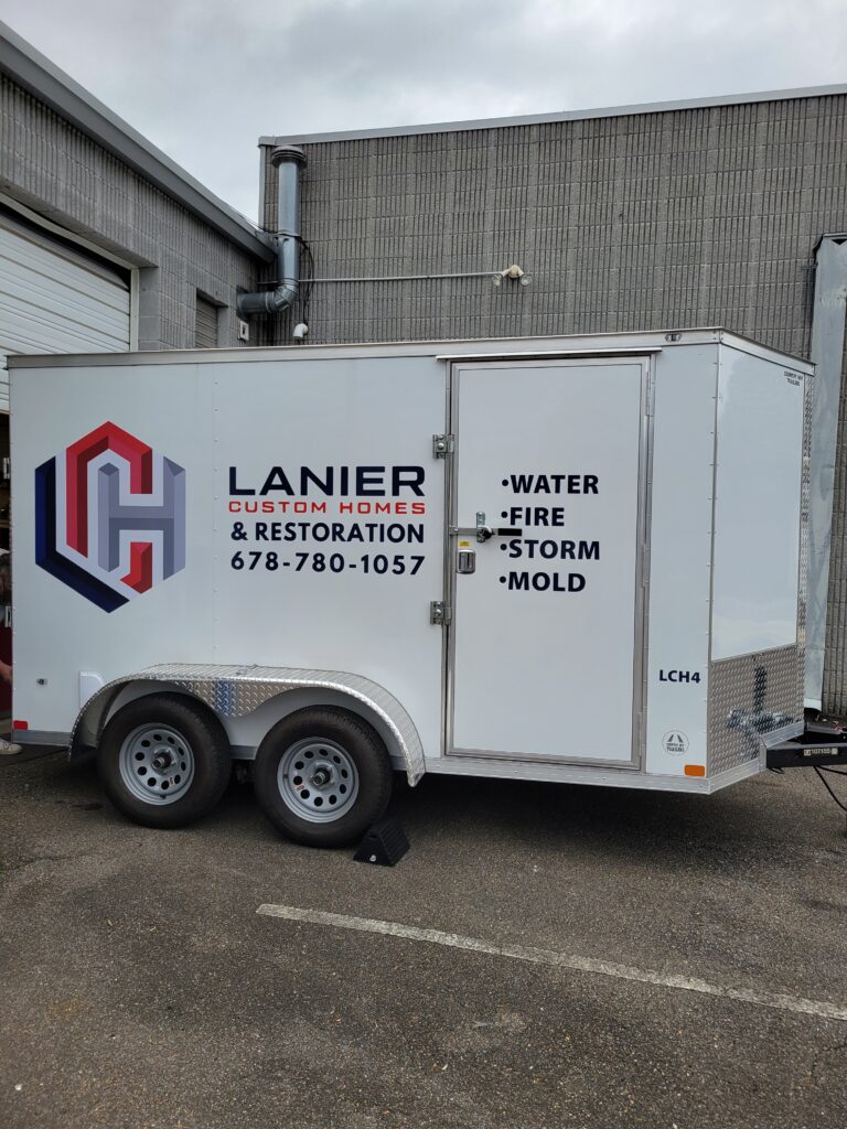 Side panel vinyl graphic installation on a white commercial equipment trailer highlighting the red, dark gray, and blue corporate geometric logo.