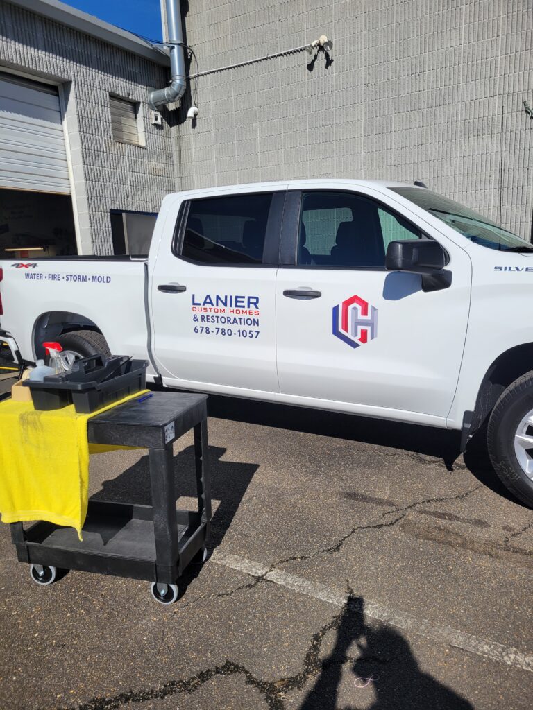 Side view of a white Chevrolet Silverado commercial truck displaying custom printed door decals with the interlocking corporate logo shield and phone number 678-780-1057.