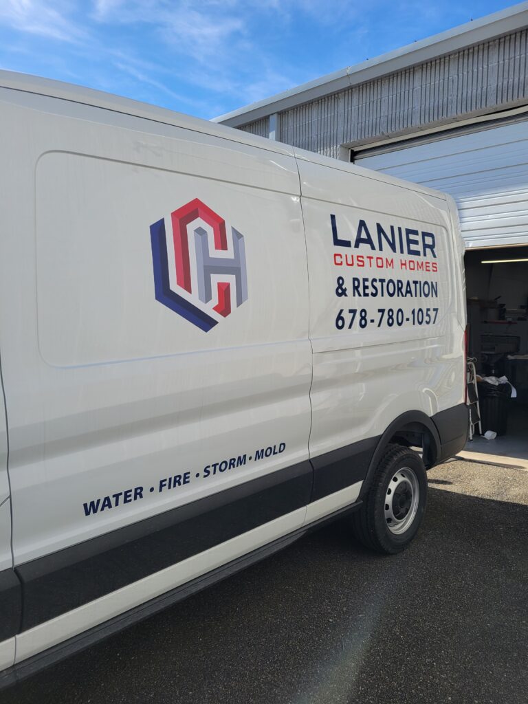 Mid-section side panel view of a white Ford Transit commercial van displaying the large multi-color interlocking Lanier logo and bold text.