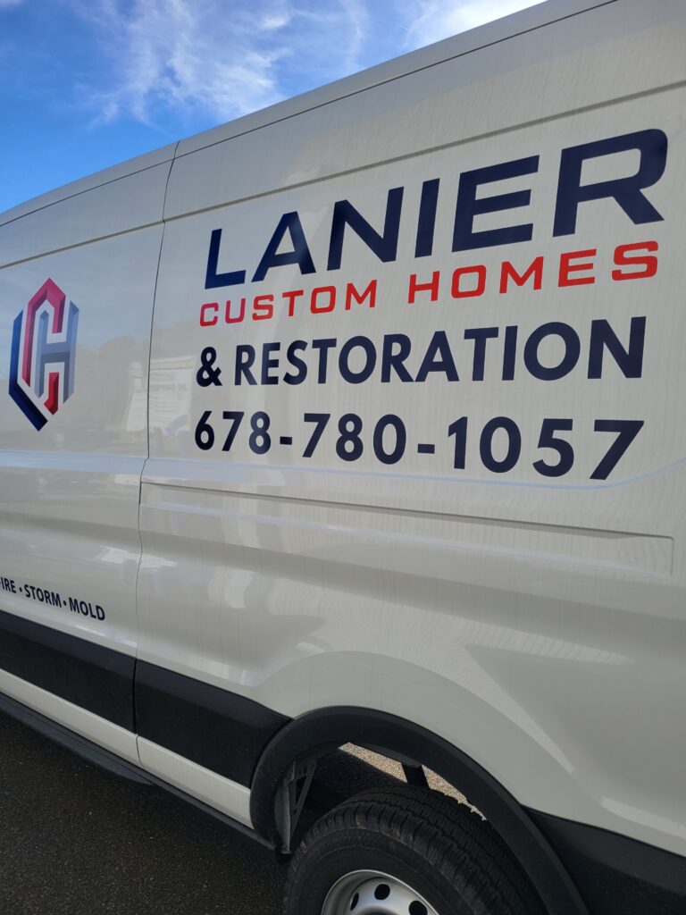 Macro detail view of crisp dark gray and red vinyl commercial lettering spelling out Lanier Custom Homes & Restoration 678-780-1057.