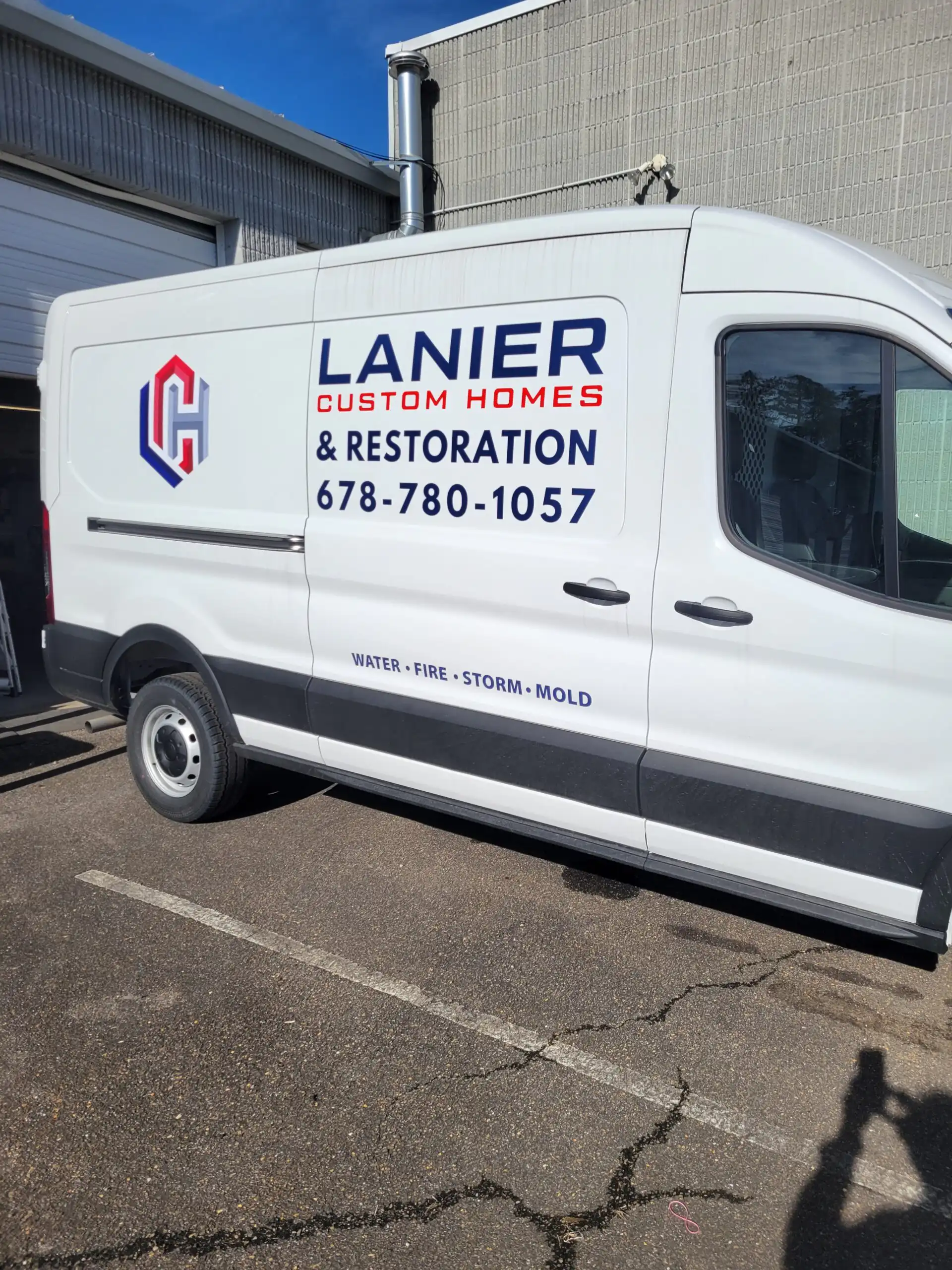 Side profile of a white Ford Transit 250 commercial service van parked outdoors, featuring clean teal, red, and navy blue vinyl fleet decals for Lanier Custom Homes.